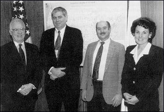 Three man and one woman posing for photo with a flag and map in background