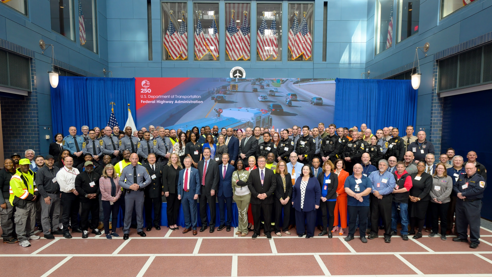 Deputy Secretary of Transportation Steven Bradbury and Federal Highway Administrator Sean McMaster with the first responders and LEOs assembled for a group photo in front of the stage in the USDOT headquarters building atrium.