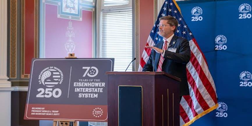 FHWA Administrator McMaster speaks while standing at a podium with Freedom 250 highway sign beside it