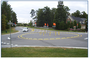 A simple roundabout created by pavement markings, armadillos (i.e., raised pavement markers), and flag-mounted delineators.