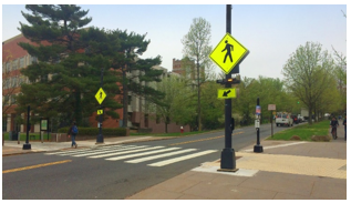 Mid-block pedestrian crossing location with crosswalk visibility enhancements including bright yellow-green pedestrian crossing warning signs and bright new pavement markings in the crosswalk.