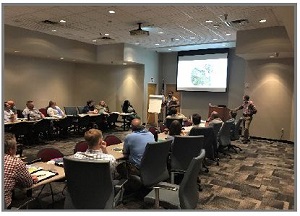 Photo shows meeting attendees watching a presentation.