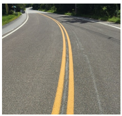 Close up of the surface of a two-lane roadway with a double yellow line that has received high friction surface treatment.