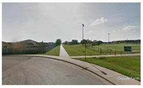 Photo depicts a closer view of the point where a pedestrian sidewalk extends forward while diverging from the roadway, which curves sharply to the left.