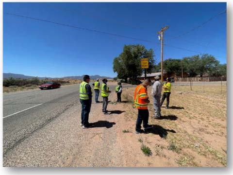 Photo of people on the side of a road wearing safety vests.