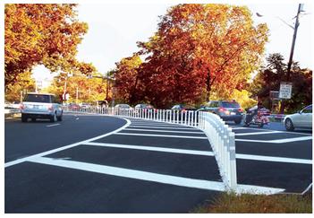 A brightly painted merge area that features bright white channelizing devices and wide road striping to outline the curvature of the traffic pattern. In this photo, two separate two-lane roadways come from different directions and curve to run parallel to each other. The four lanes are separated by a series of channelizing devices.