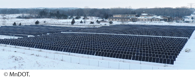 "Rows of solar panels in an open field surrounded by snow. Nearby are buildings and trees. Image Source: © MnDOT."