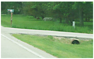 A drainage pipe crosses below a driveway on a rural road, allowing run-off water to flow in the ditch that bisects the driveway.