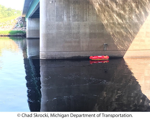 An unmanned surface vehicle in the water beside a bridge pier. © Chad Skrocki, Michigan Department of Transportation.