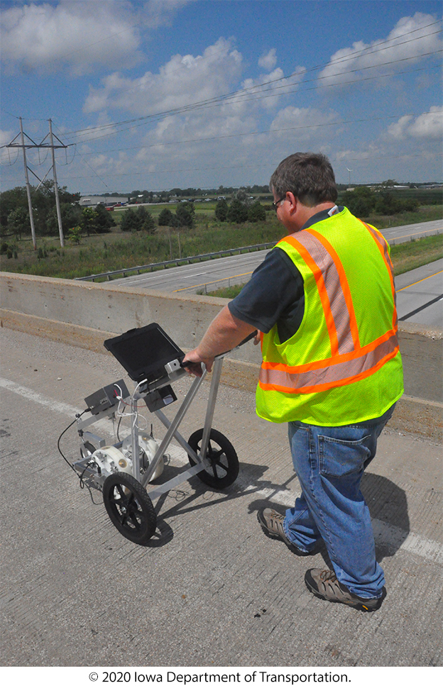 A man pushes equipment in a small cart on a bridge. © 2020 Iowa Department of Transportation.