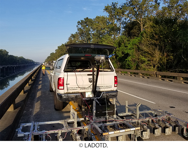 A truck on the side of a bridge pulls nondestructive evaluation equipment behind it. © LADOTD.