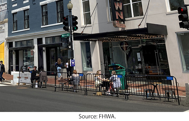 A fenced area on the roadway beside the curb has a few outdoor dining tables. Source: FHWA.