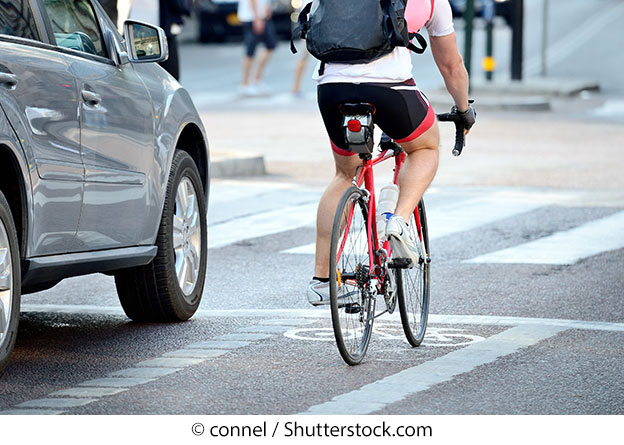 A bicyclist beside a car on a roadway. © connel / Shutterstock.com