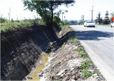 "This photo shows a deep, v-shaped, muddy drainage ditch."