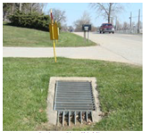 "A drainage pipe that bisects a driveway and has a concrete sleeve and grating covering the opening to prevent vehicles from dropping into it."