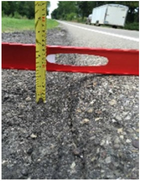 "Shows the edge of a paved roadway with a level and ruler. The roadway has a slanted edge due to the SafetyEdge treatment."