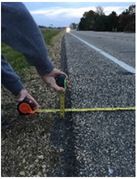 "Shows the edge of a paved roadway with a level and ruler. The roadway has a standard edge."