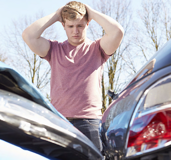 "teenager with hands on head looking down at the damage done to his car and another car"