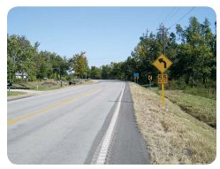 "Photo of a rural roadway with a curve warning sign near the side of the roadway."