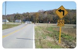 "Photo of a curve warning sign in advance of a 90 degree curve. The sign also indicates the maximum safe speed limit on the curve is 20 mph."