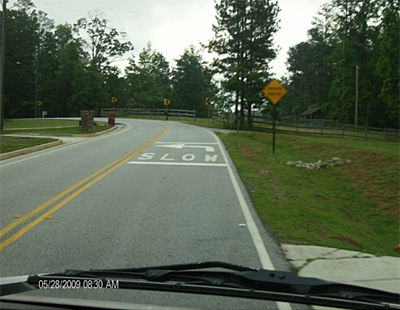 "Figure 4: Photo. This photo shows a view of CURVE AHEAD pavement markings and signage from a car. The pavement marking is the word SLOW and a curve arrow preceding the curve. The sign is a yellow diamond that says CURVE AHEAD."