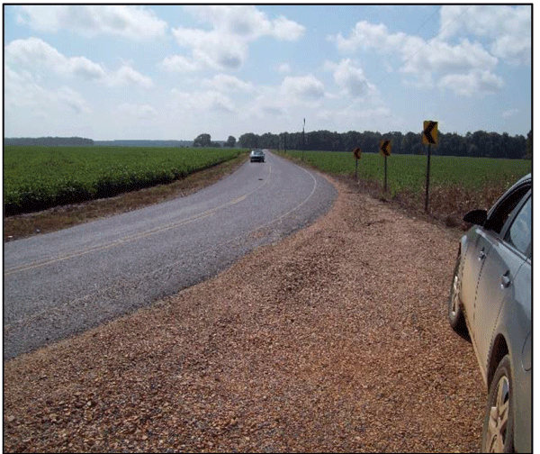 Close-up photograph showing an intersection within a horizontal curve with aggregate scattered on paved roadway.