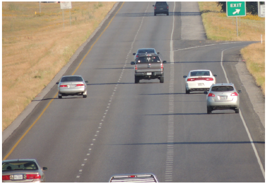 Figure 56. A picture showing half of a section of a four-lane freeway containing an approach to a freeway exit ramp.  The left edge of the auxiliary lane into the exit ramp is defined by white dotted lane line markings.