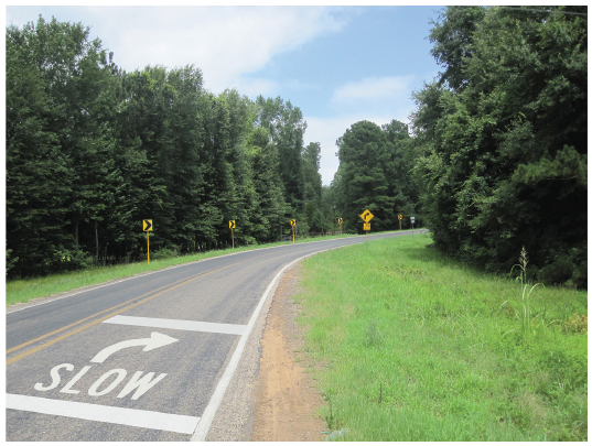 Figure 58. A picture of an approach to a horizontal curve on which the word 'SLOW', a right arrow, and two white transverse lines have been painted on the pavement surface.