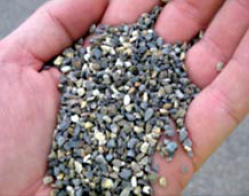 A man's hand holding calcined bauxite gravel, which appears to average about 4 mm in size, in the palm. 