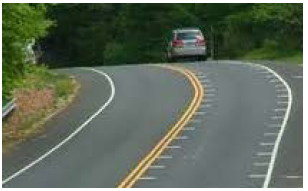 "Curving roadway featuring optical speed bar markings on the pavement at each edge of the travel lane."