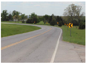"Series of post-mounted chevrons on the side of a curving road."