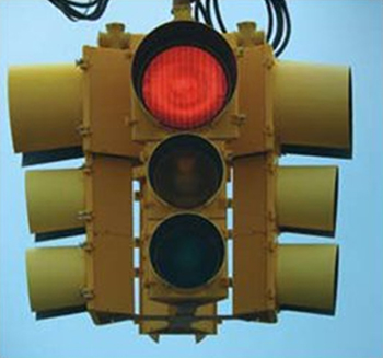 ""Photograph of a 4-way signal head in which the red light lens is 12 inches in diameter and the yellow and green lenses below it are 8 inches in diameter.