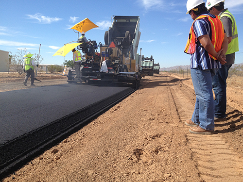 "Photograph of a paving crew laying down a coat of asphalt"