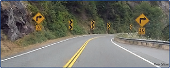 "US 199 in Del Norte County on the approach to a horizontal curve with curve warning signs, chevrons, and advisory speed placards. Photo courtesy of Caltrans."