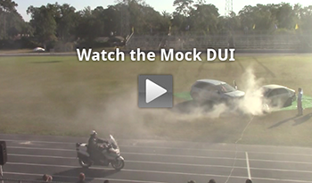 "Screen capture from the safety video shows two cars crashing on a high school field. There is a 'play' button graphic atop the photograph to signify that this image is linked to the video."