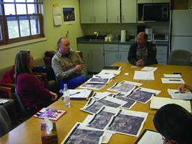 Photo. RSA start-up meeting. Participants in a start-up meeting sit around a table looking at photos of the project location.