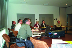 Photo. Preliminary findings meeting. Members from a project owner/design team sit in a room listening to a presentation from RSA audit team members.