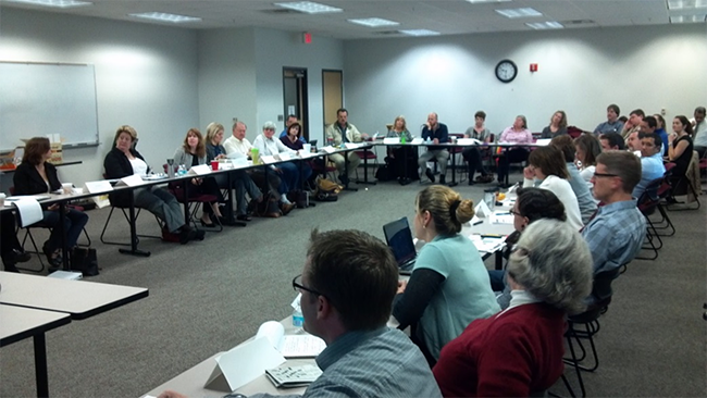 "photo of the quarterly meeting members sitting at tables arranged in a 'U' shape"