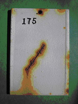 Photo. This closeup of panel 175, which is an SSPC-SP3 surface with an MCU2 overcoat after exposure outdoors for 24 months, shows a moderately rusted scribe diagonally across the panel, with small blisters all over the surface.