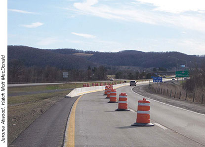 Traffic control in this work zone on a New York interstate involved marking the transition from two-lane traffic to one lane, using orange drums and a temporary concrete barrier.