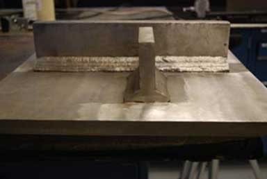 "The photograph consists of a large metal surface showing two smaller rectangular metal plates that have been welded in place. The longer metal plate is horizontally positioned in the photograph, with the shorter metal plate placed perpendicularly. The welds joining the edges of the smaller plate to the rectangular surface are clearly visible."