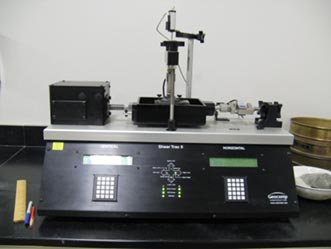 Figure 9. This is a photo showing a front view of a standard direct shear device. There are controllers on the bottom with the shear box on the top, connected to a motor and a load cell.