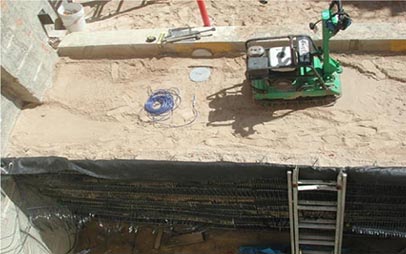 Figure 12. Top-down view showing into the outdoor geotechnical sand pits. A mechanically stabilized earth (MSE) shoring wall is on one side and a green lightweight vibratory compactor is shown on top of the sand.