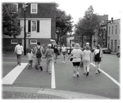 Pedestrians walking through intersection with buildings and trees on either side of street