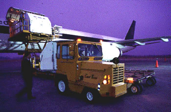 A plane on runway being loaded with yellow cargo truck at night