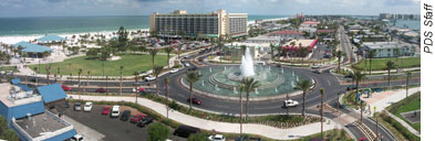 A roundabout shown in Clearwater, Florida with buildings and vehicles in surrounding areas with water in the background