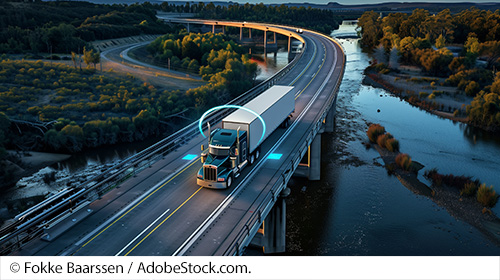 Semi-truck driving on two-lane rural highway with illuminated sensors mapping space around truck’s wheels and freight. Image Source: © Fokke Baarssen / AdobeStock.com.