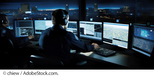 Two men wearing headsets watch traffic at night on several TV monitors while overlooking a cityscape. Image © chiew / AdobeStock.com.