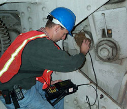 An inspector wearing a blue hard hat is checking a steel bridge pin.