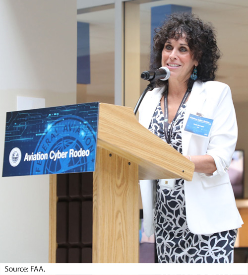 A woman speaks to an audience from a podium inside of a meeting room. Image Source: FAA.